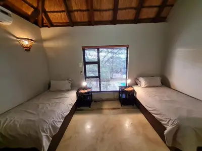two beds in a room with a window at Pumba's Place Zebula 6 Bedroom House in Mabula