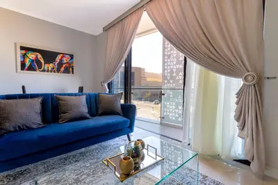 a living room with a blue couch and a large window at Alimama Spaces: The Chelsea's Ellipse in Midrand