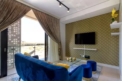 a living room with a blue couch and a large window at Alimama Spaces: The Fountain Hill Ellipse in Midrand
