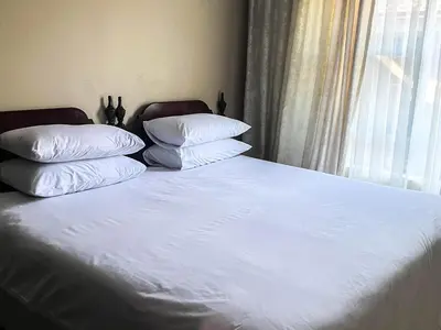 a bed with white sheets and pillows next to a window at Tshamani self catering in Hazyview