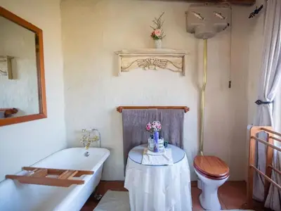 a bathroom with a tub and a toilet and a table at Glen Aden in Dullstroom