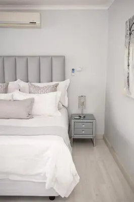 a white bedroom with a bed and a side table at Augusta Palms in Centurion