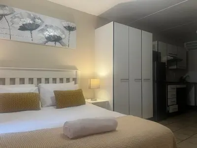 a bedroom with a large white bed and a kitchen at Smart and Cozy Studio with Netflix and Showmax in Pretoria