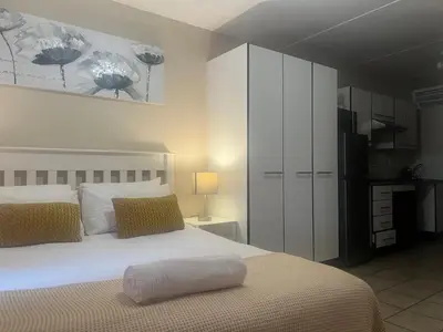 a bedroom with a large white bed and a kitchen at Smart and Cozy Studio with Netflix and Showmax in Pretoria