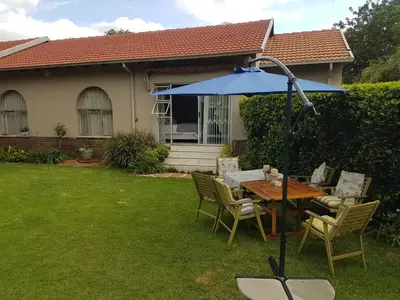 a table and chairs with a blue umbrella in a yard at Roosboompies Guest Suite in Centurion