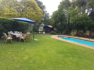 a yard with a table and an umbrella next to a pool at Roosboompies Guest Suite in Centurion