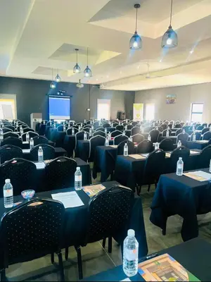 a conference room with tables and chairs and a screen at Ndalo Lodge Oshoek in Oshoek