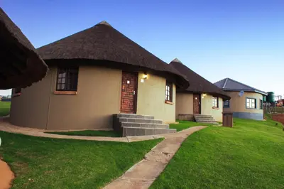 a small house with a thatched roof on a lawn at Ndalo Lodge Oshoek in Oshoek
