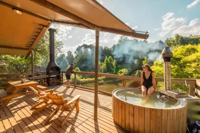 a woman sitting in a hot tub on a deck with a fireplace at AfriCamps Magoebaskloof in Magoebaskloof