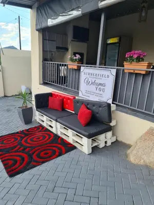 a bench with red pillows sitting outside of a house at SummerField Guest House in eNyamazaneni
