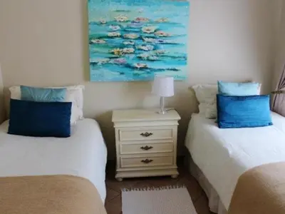 a bedroom with two beds and a dresser with a painting at Dullstroom Artist Cottages in Dullstroom