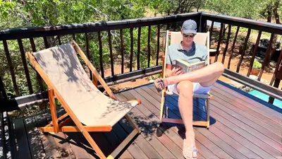 a man sitting in a chair reading a book on a deck at Kruger Kumba - Mugwenzi in Marloth Park