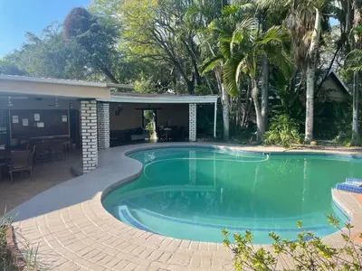 a swimming pool with a patio and a house at Rosscos Lodge in Phalaborwa