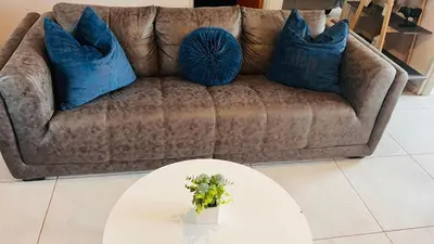 a couch with two blue pillows and a white table at Zinathi Lodge in Polokwane