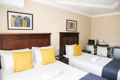 two beds in a hotel room with yellow pillows at M n M Guesthouse Polokwane Central in Polokwane