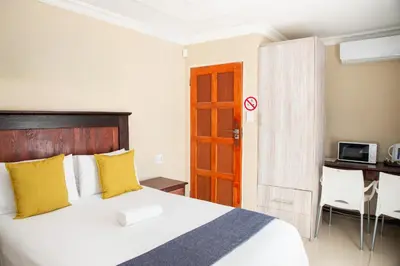 a bedroom with a bed with yellow pillows and a desk at M n M Guesthouse Polokwane Central in Polokwane