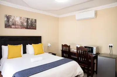 a bedroom with a bed with yellow pillows and a desk at M n M Guesthouse Polokwane Central in Polokwane