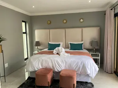 a bedroom with a large bed with two ottomans at The King's Court Guest Manor in Bela-Bela