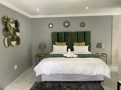 a bedroom with a large bed with a green headboard at The King's Court Guest Manor in Bela-Bela