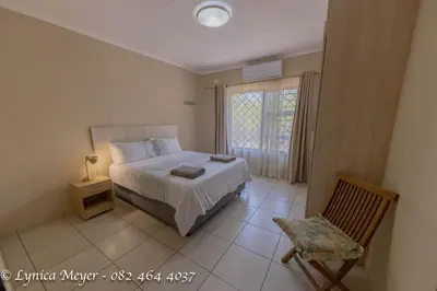 a bedroom with a bed and a chair and a window at Mamba Bush House in Marloth Park