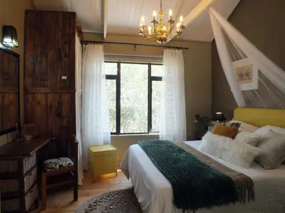 a bedroom with a bed with a chandelier and a window at Pheasant's Crest in Marloth Park