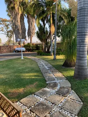 a stone walkway in a park with palm trees at Cottage 32 in Groblersdal