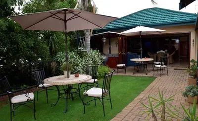 a patio with tables and chairs and an umbrella at LUXURY EN-SUITE ROOM WITH LOUNGE @ 4 STAR GUEST HOUSE in Middelburg