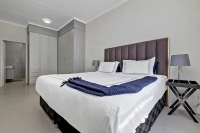a large white bed with a blue blanket on it at Smart Apartment in Midrand