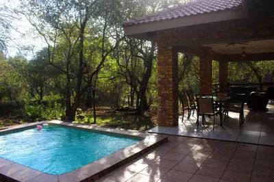 a swimming pool in a patio with a table and chairs at Nature House in Marloth Park