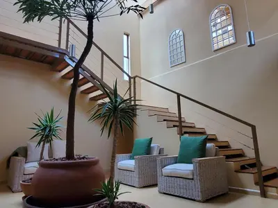 a lobby with a staircase with chairs and palm trees at Avonlea Guesthouse in Polokwane