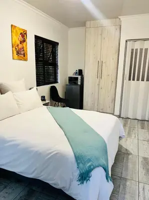 a bedroom with a white bed with a blue blanket on it at Zindiza Guesthouse in Witbank