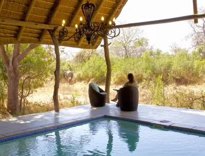a woman sitting in a chair next to a swimming pool at Kambaku River Sands in Timbavati Game Reserve