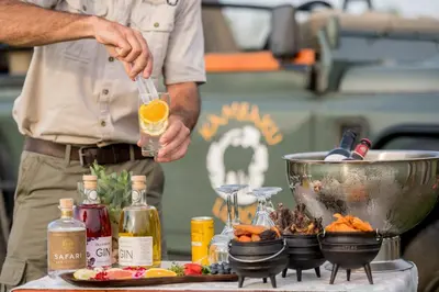 a man holding a glass of wine next to a table with food at Kambaku River Sands in Timbavati Game Reserve