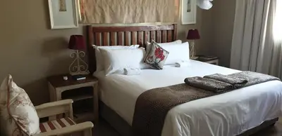 a bedroom with a bed with white sheets and a chair at Stoep Cafe Guest House in Komatipoort