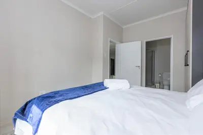 a white bed with a blue blanket on top of it at Smartz Apartment 334 in Midrand
