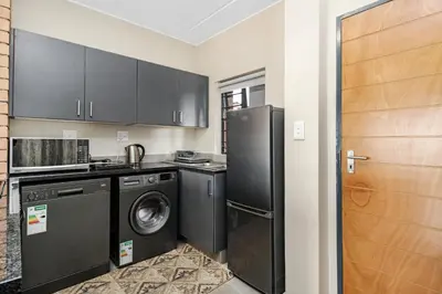 a kitchen with black cabinets and a washer and dryer at Smartz Apartment 334 in Midrand