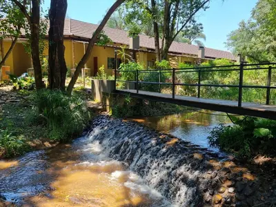 a bridge over a stream in front of a house at Aan De Vliet Holiday Resort in Hazyview