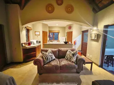 a living room with a brown leather couch and a kitchen at 10 Raptors Lodge in Hoedspruit