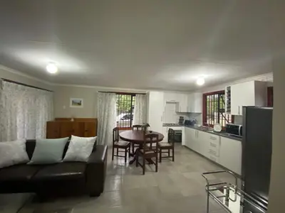 a living room with a couch and a table and a kitchen at Man and Dog Log Cabin in Midrand