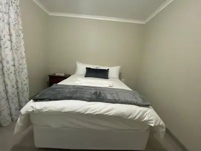 a white bed with a black pillow on top of it at Man and Dog Log Cabin in Midrand