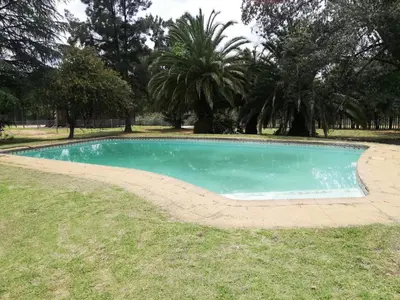 a swimming pool in the grass with trees in the background at Man and Dog Log Cabin in Midrand