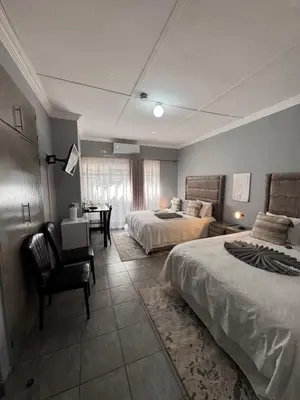 a bedroom with two beds and a chair and a desk at President Guest Lodge in Louis Trichardt