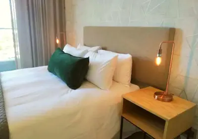 a bed with white pillows and a table with a lamp at Menlyn Apartment - Trilogy in Pretoria