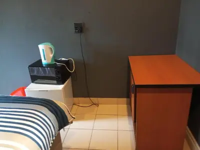 a room with a bed and a desk with a cup on top at Aloha Menlyn Lodge Ensuite Rooms with shower all with own entrance and unlimited free WiFi in Pretoria