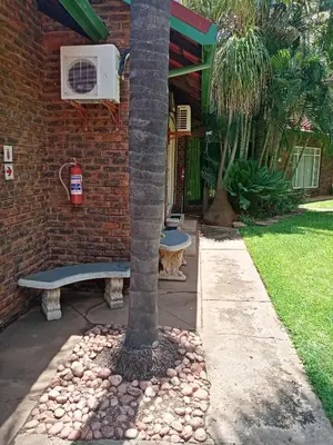 a tree and a bench next to a brick building at De la Rose Guesthouse in Lephalale