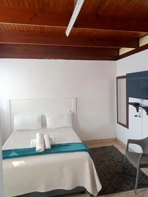 a white bedroom with a bed and a chair at PARK FRONT LODGE in Polokwane