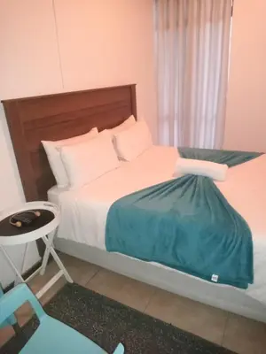 a bedroom with a bed and a table and a chair at PARK FRONT LODGE in Polokwane