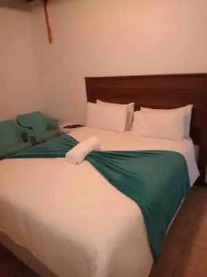 a bedroom with a large bed with a green blanket at PARK FRONT LODGE in Polokwane