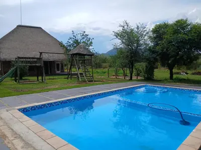 a blue swimming pool with a playground and a house at Bossi Lodge in Hartbeespoort