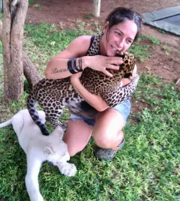 a woman holding a cheetah and a white cat at Simba Safaris African Pride Exotic Lodge in Lephalale